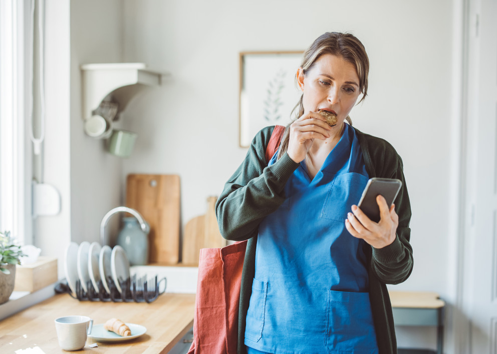Care giver using her mobile device while eating breakfast
